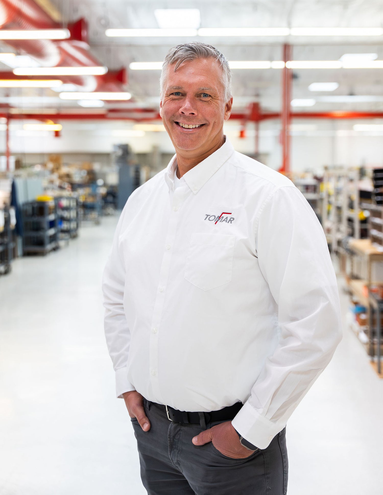 Adam Miller wearing a white shirt with a TOMAR Logo in a warehouse setting